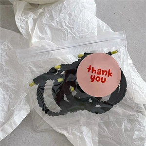 Détail d'élastiques à cheveux ondulés noirs en sac zippé avec autocollant de merci