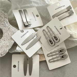 Close-up of geometric matte silver hair clips in rectangle and wave shapes on card