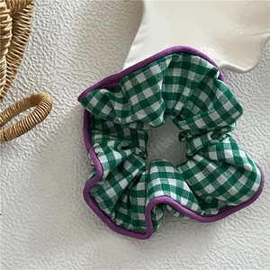Détail d'un chouchou à carreaux verts avec bordure violette sur fond blanc