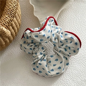 Détail du chouchou en tissu blanc avec motifs floraux bleus et bordure rouge contrastée