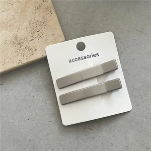 Close-up of matte silver rectangular hair clips on a white display card minimalist style