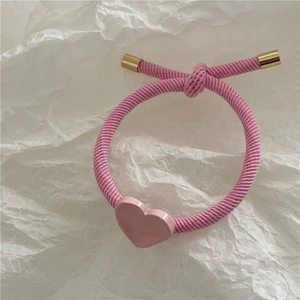 Close-up of pink ribbed elastic hair tie featuring a golden metal tip and heart pendant