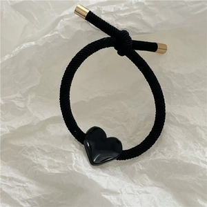 Close-up of black elastic hair tie featuring a glossy heart charm and gold metal caps