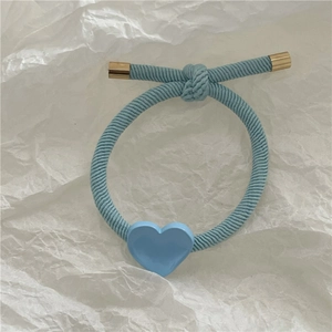 Detail of light blue twill hair tie featuring a polished golden heart pendant and metal caps