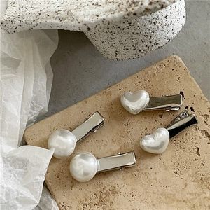 Detail shot of four silver hair clips featuring heart and round faux mabe pearls on stone