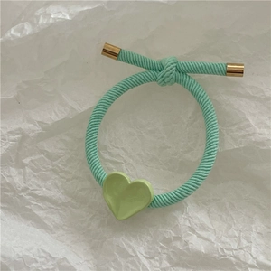 Detail of mint green braided hair tie featuring a heart charm and gold metal accents