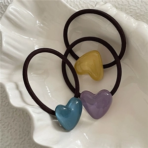 Three colorful resin heart charms on dark brown elastic hair ties in a shell dish