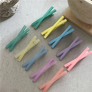 Gros plan de pinces à cheveux en forme de X colorées aux tons pastel mats sur pierre