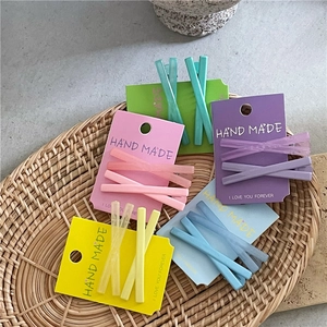Gros plan de pinces à cheveux en X mates en cinq couleurs macaron sur un plateau tressé
