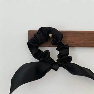 Detail of elegant black satin hair scrunchie with long ribbon bow on wooden hook