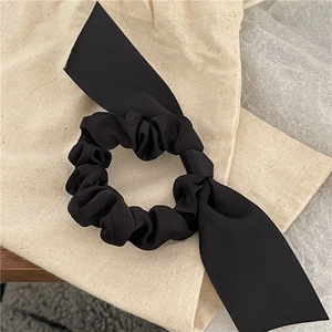 Detail of a black satin ribbon scrunchie with a soft pleated texture and elegant long streamers