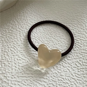 Detailed macro view of a champagne resin heart pendant on a black elastic hair tie