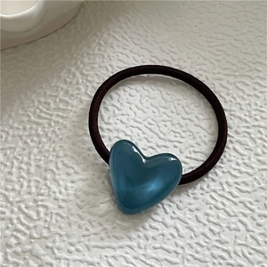 Detailed view of elastic hair tie with blue resin heart pendant on textured background