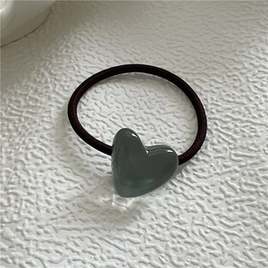 Detail of a Morandi green heart-shaped resin charm on an elastic black hair tie band