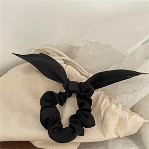 Elegant black satin scrunchie with rabbit ear bow on a minimalist aesthetic background