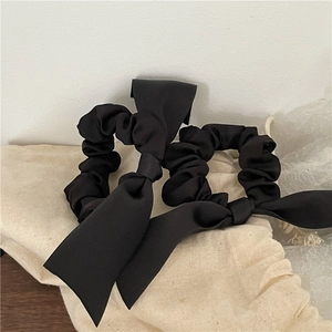 Detail of two black fabric scrunchies with long bow ribbons on a minimalist background