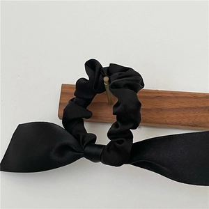 Elegant black satin bow scrunchie with long ribbons on a wooden stand for hair styling