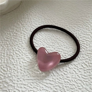 Detail of a brown elastic hair tie featuring a smooth pink heart resin decoration