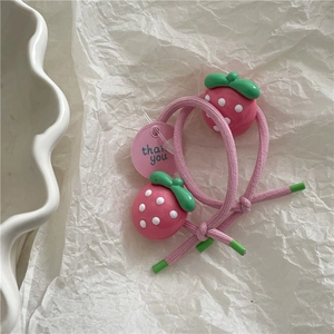 Close-up of pink elastic hair ties with strawberry pendants on a white paper background