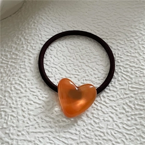 Detailed close-up of amber orange heart charm on coffee brown high elastic hair tie
