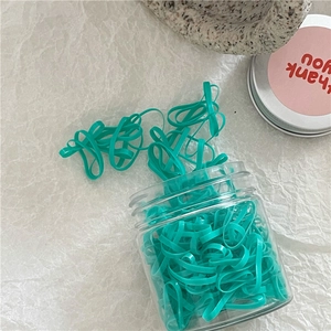 Close-up of cyan elastic hair ties in transparent storage jar on textured paper