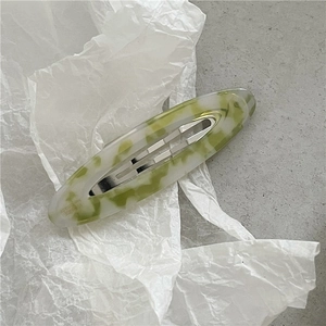 Detail view of oval acetate hair clip featuring green and white marble textures