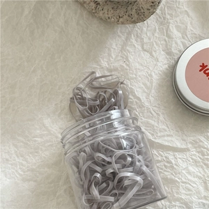 Close-up of grey high-elastic hair bands in a transparent jar on aesthetic paper background