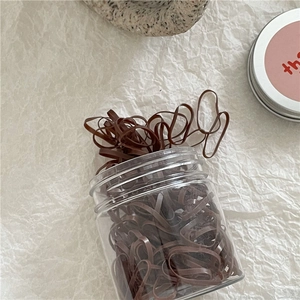Detail view of brown elastic hair bands neatly packed in a clear jar on white paper