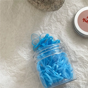 Close-up of blue high-elasticity hair ties in a clear round jar on a minimalist background