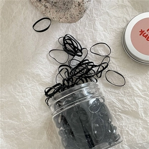 Close-up of black elastic hair bands stored in a clear jar on a textured background
