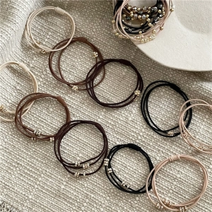 Détail de chouchous élastiques perlés en crème, marron et noir sur tissu texturé