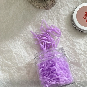 Detail view of purple high-elasticity hair ties spilling from a clear round plastic jar