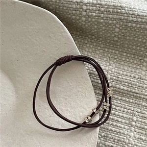 Détail d'un élastique à cheveux triple marron foncé avec anneaux dorés et strass brillants