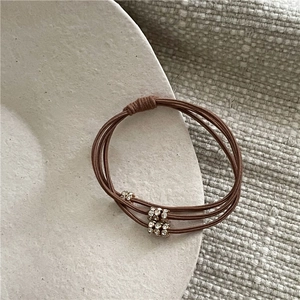 Détail d'un élastique à cheveux avec trois perles en métal serties de strass en marron café