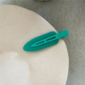 Detailed macro view of a matte teal water drop hair clip on a beige ceramic plate surface