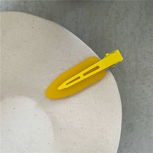 Close-up of a translucent yellow hair clip on a minimalist stone plate with grey background