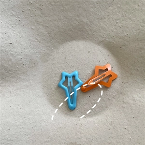 Detail of star-shaped snap hair clips in blue and orange with matte lacquer finish