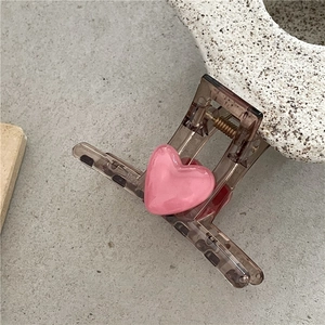 Brown translucent hair claw clip with pink heart decoration on grey stone background