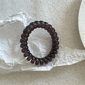 Gros plan d'un élastique spirale marron foncé translucide sur fond texturé blanc