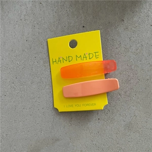 Détail de deux pinces à cheveux rectangulaires orange et pêche sur carte jaune