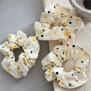 Trois chouchous crème à pois colorés présentés sur un set de table tressé naturel