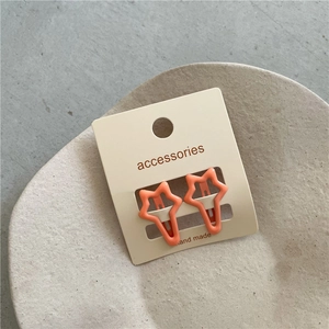 Detail of two orange star-shaped hair clips on a white card in a stone tray