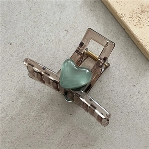 Close-up of a brown transparent hair claw clip with a green cat-eye stone heart detail