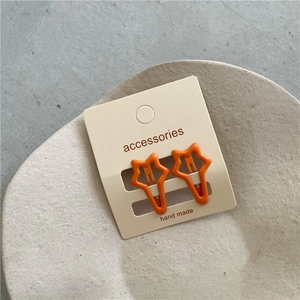 Close-up of two orange star-shaped metal hair clips on a handmade card holder