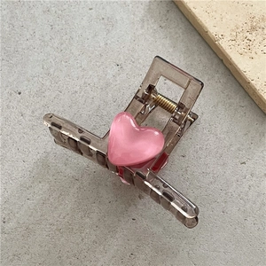 Macro view of transparent brown hair claw clip with a pink opal heart and golden spring