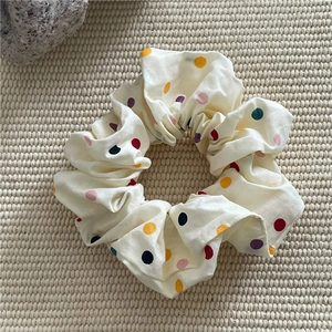 Vue détaillée d'un chouchou crème à pois colorés sur une texture de fond tissée