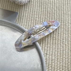Dettaglio di un fermaglio per capelli BB in acetato marmorizzato blu e rosa su vassoio