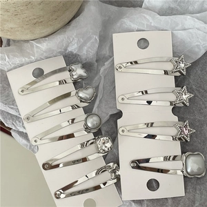 Horquillas plateadas con pedrería de corazón y perlas en un cartón de presentación