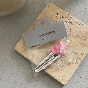 Détail de la barrette argentée avec cœur rose en strass sur une carte de présentation