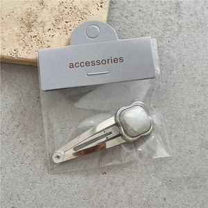 Detalle de pinza para el pelo de metal plateado con piedra crema sobre tarjeta de soporte